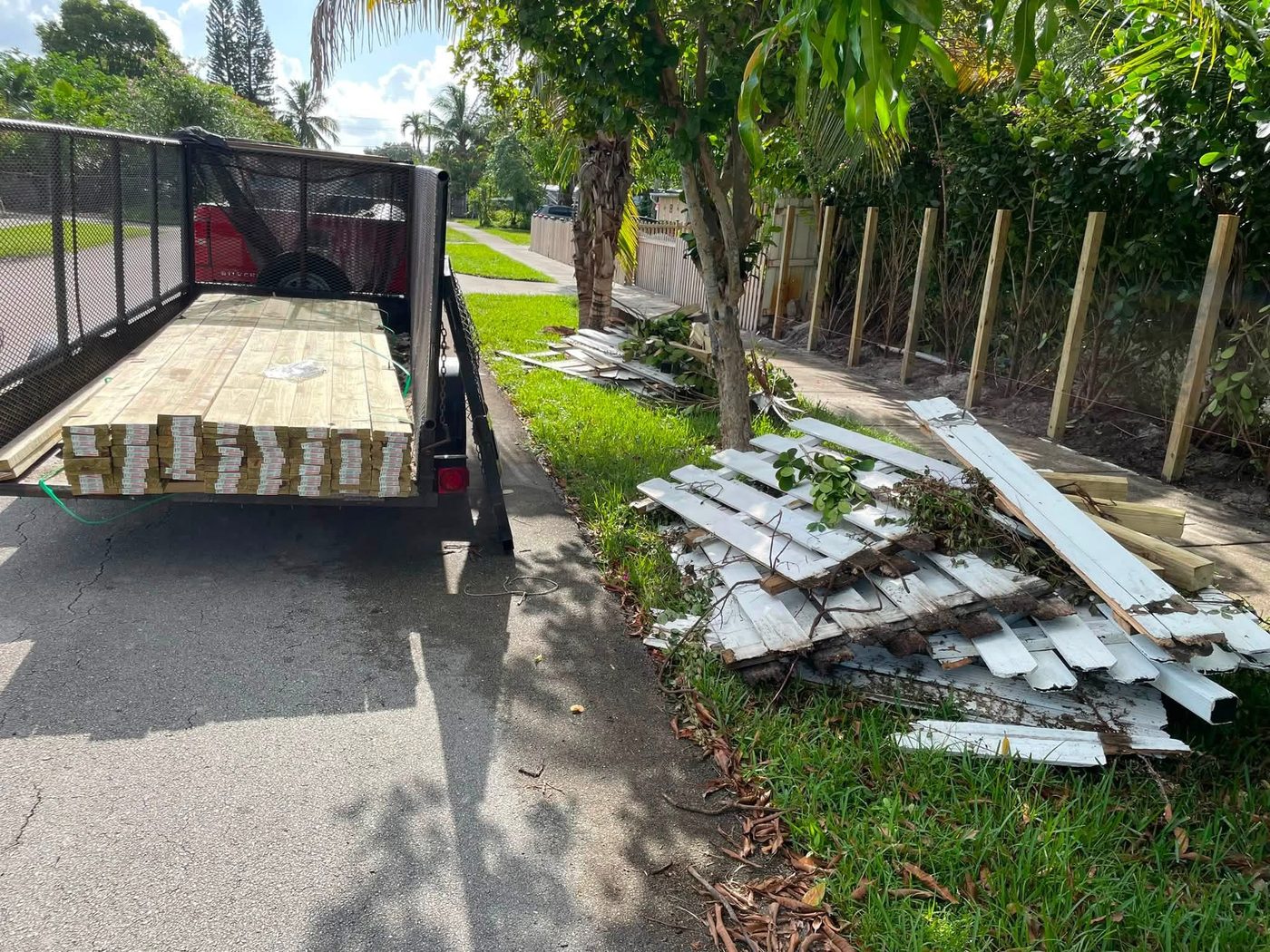 Trailer loaded with fence lumber next to a property with new fence posts set