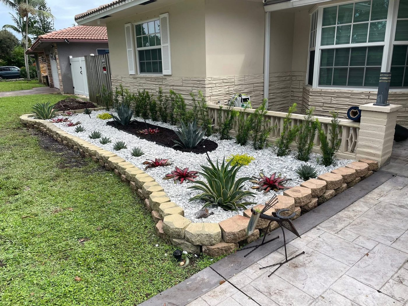 Completed front-yard landscape bed with white river rock, agave, and bromeliads