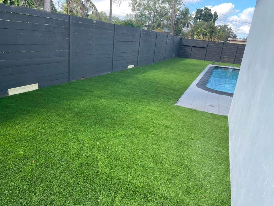 Backyard with completed synthetic grass installation, wood privacy fence, and pool